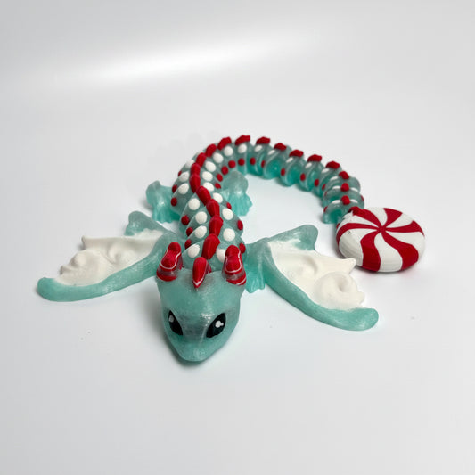 A 3d printed dragon figurine made from translucent mint plastic, decorated with red and white beads along its back and tail, white wings, and a red-and-white striped candy accessory.