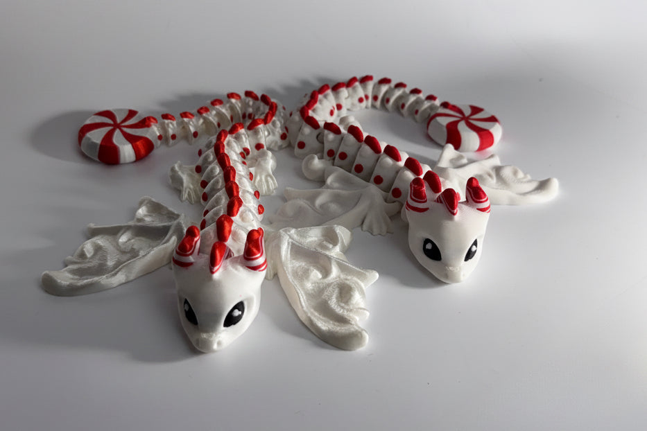 A small white dragon figurine with red accents, including red spots along its back, red horns, and red-and-white striped tail pieces, displayed on a plain light gray background.